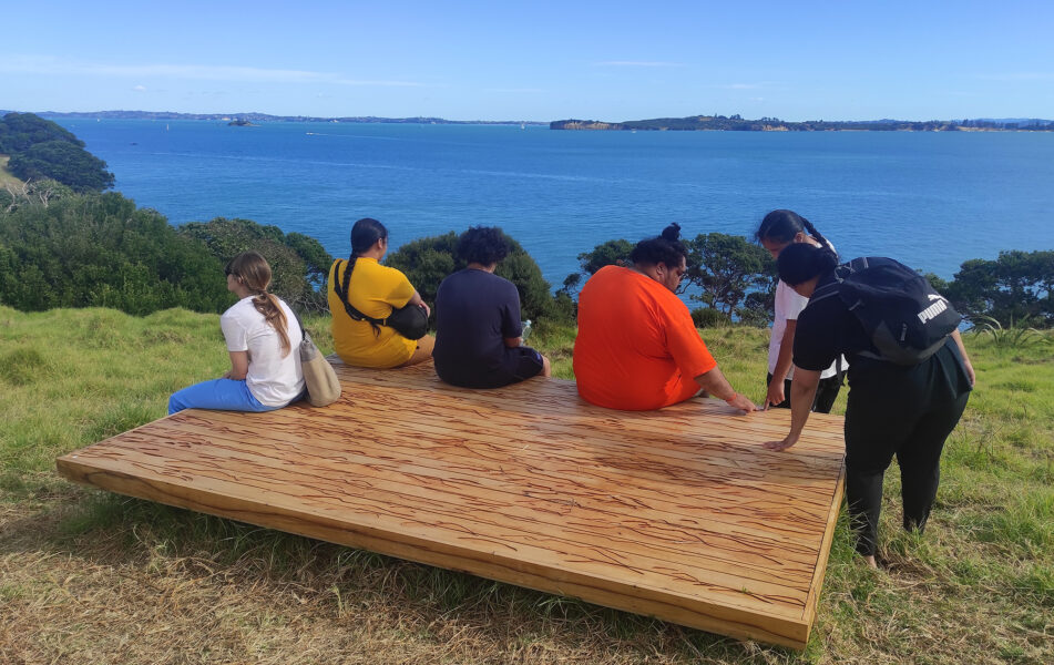 6 people with their backs to camera sitting on platform looking at sea